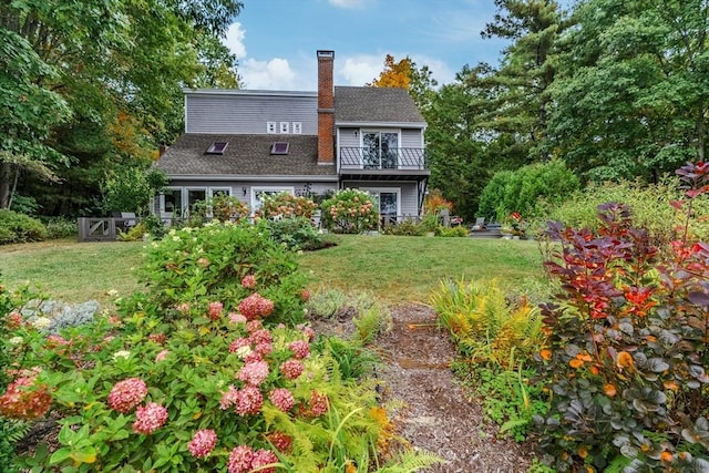 rear view of house with a lawn, a balcony, and a chimney