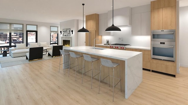 kitchen with a center island with sink, light stone counters, light hardwood / wood-style floors, and pendant lighting