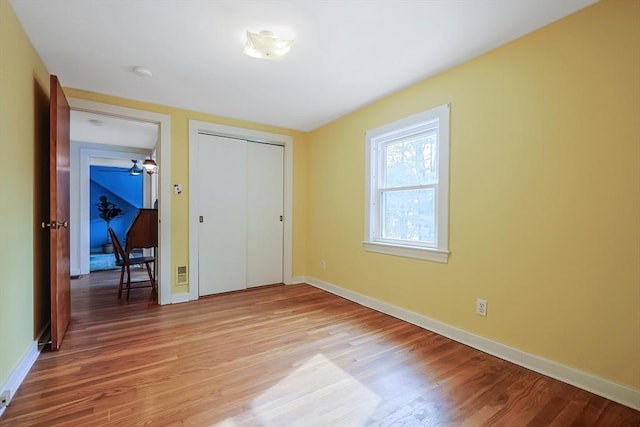 unfurnished bedroom featuring a closet, visible vents, baseboards, and wood finished floors