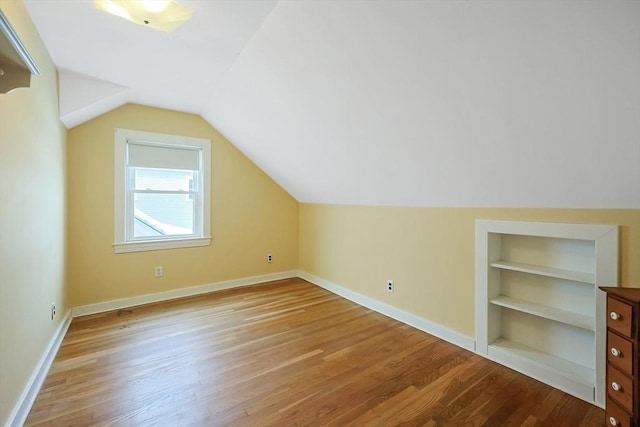 bonus room with light wood finished floors, baseboards, built in features, and vaulted ceiling