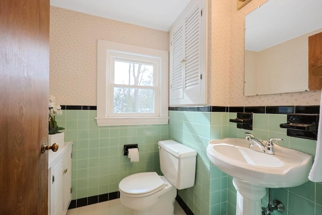 half bathroom featuring a wainscoted wall, toilet, and wallpapered walls