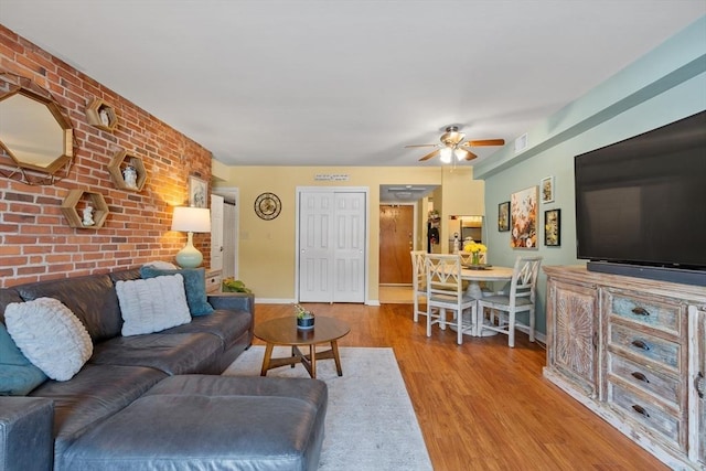 living room with light hardwood / wood-style floors, ceiling fan, and brick wall