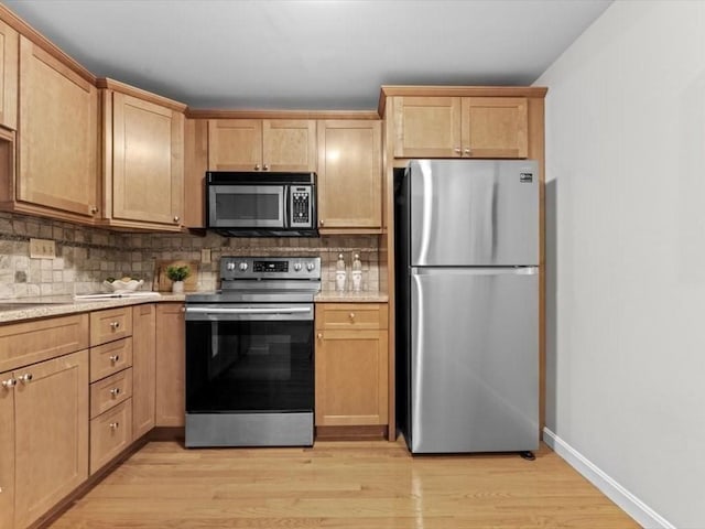 kitchen with appliances with stainless steel finishes, decorative backsplash, light wood finished floors, baseboards, and light brown cabinetry