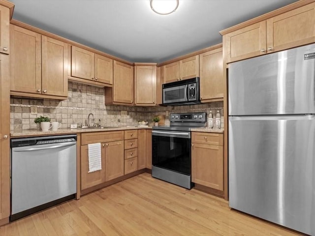 kitchen featuring stainless steel appliances, a sink, light wood-style flooring, and tasteful backsplash