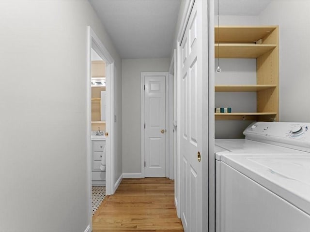 clothes washing area featuring washing machine and dryer, light wood-type flooring, and baseboards