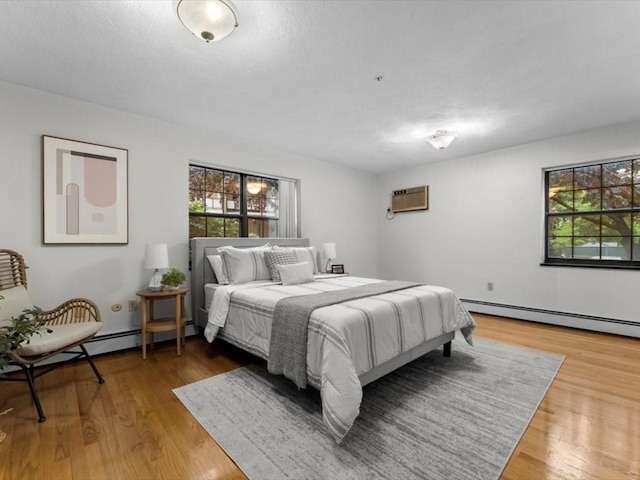 bedroom featuring a wall unit AC, wood finished floors, and a baseboard radiator