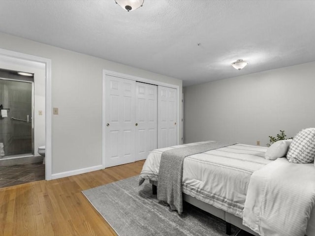 bedroom with wood finished floors, a closet, baseboards, ensuite bathroom, and a textured ceiling
