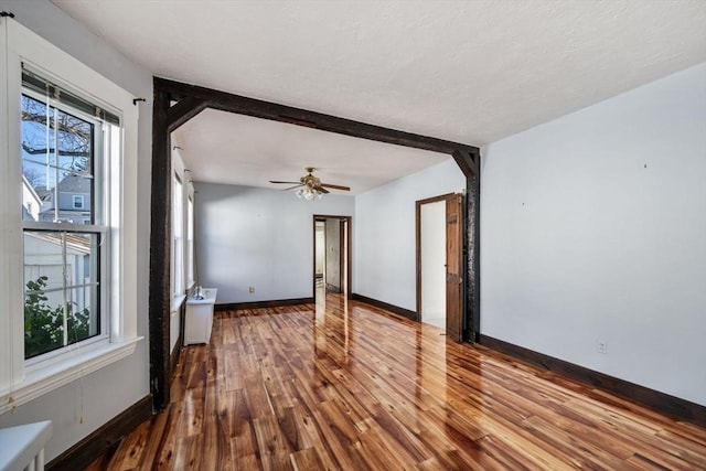 unfurnished room featuring beamed ceiling, ceiling fan, and hardwood / wood-style floors