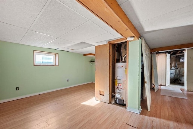 basement with a paneled ceiling, wood-type flooring, and water heater