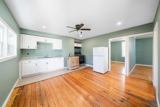 kitchen featuring black gas stove, light hardwood / wood-style flooring, ceiling fan, white fridge, and white cabinetry