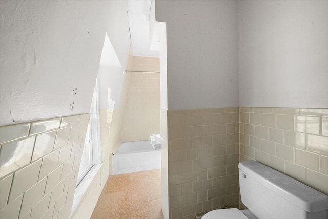 bathroom with a bathtub, toilet, and tile walls