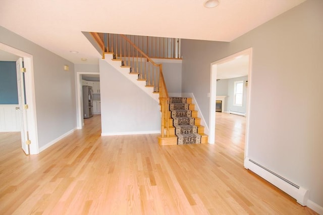 interior space with a baseboard heating unit, a glass covered fireplace, wood finished floors, baseboards, and stairs