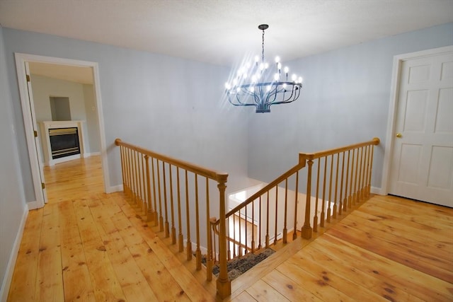 stairs with a glass covered fireplace, baseboards, an inviting chandelier, and wood-type flooring