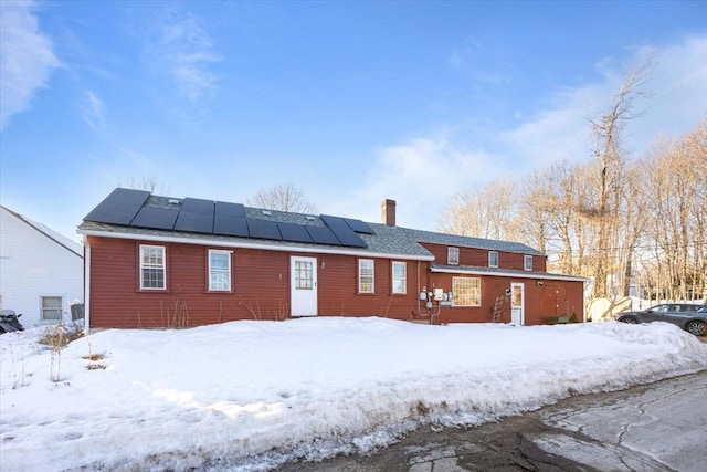 snow covered back of property with roof mounted solar panels and a chimney