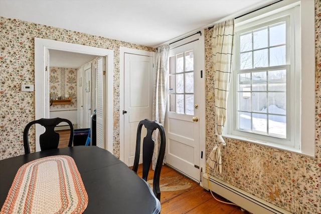 dining area with baseboard heating, wood finished floors, and wallpapered walls