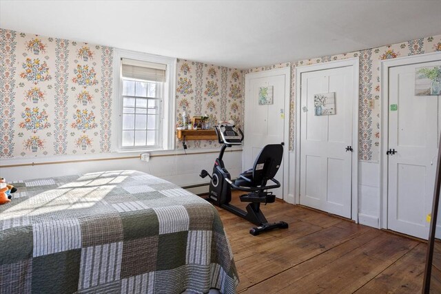 bedroom with a baseboard heating unit, wood finished floors, and wallpapered walls