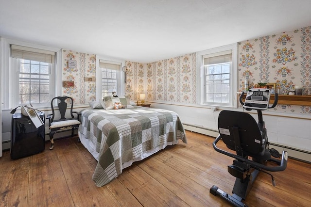 bedroom featuring wainscoting, hardwood / wood-style floors, a baseboard radiator, and wallpapered walls