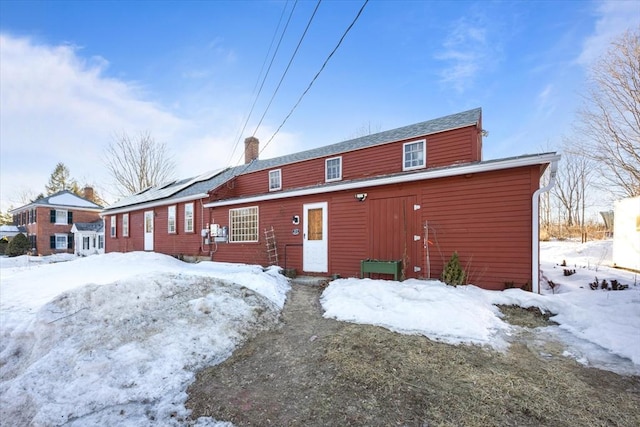 snow covered back of property featuring a chimney