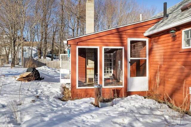 view of snow covered exterior with a chimney and fence