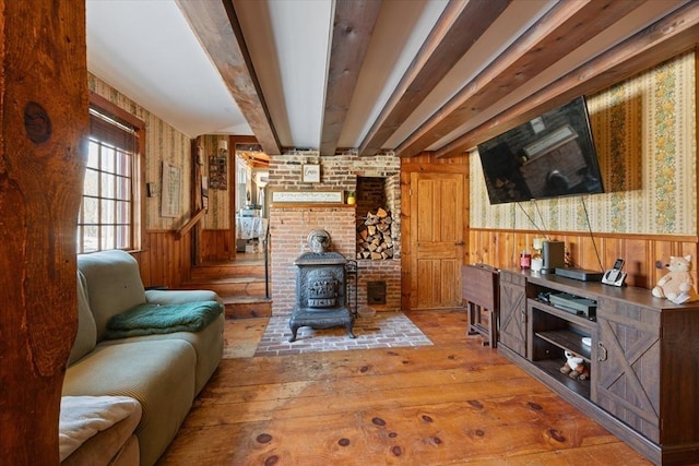 living room featuring a wood stove, wainscoting, wood-type flooring, and beam ceiling