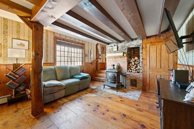 living area featuring wood walls, beamed ceiling, wainscoting, and a wood stove