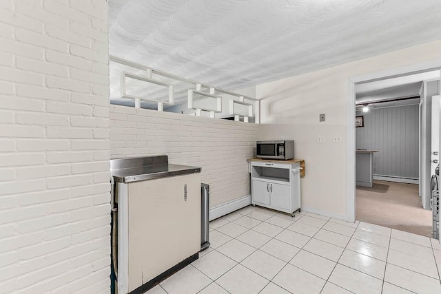 kitchen featuring brick wall, baseboard heating, light tile patterned floors, baseboards, and stainless steel microwave