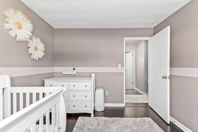 bedroom featuring a nursery area, baseboards, and dark wood-type flooring