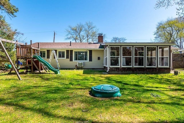 back of property with fence, a sunroom, a chimney, a playground, and a lawn