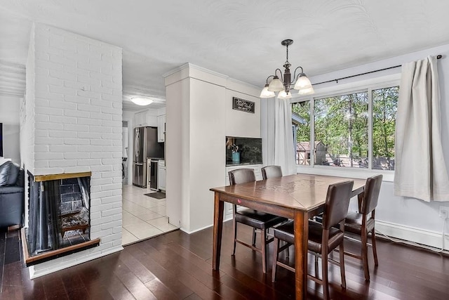 dining area with a brick fireplace, baseboards, a chandelier, and dark wood-style floors