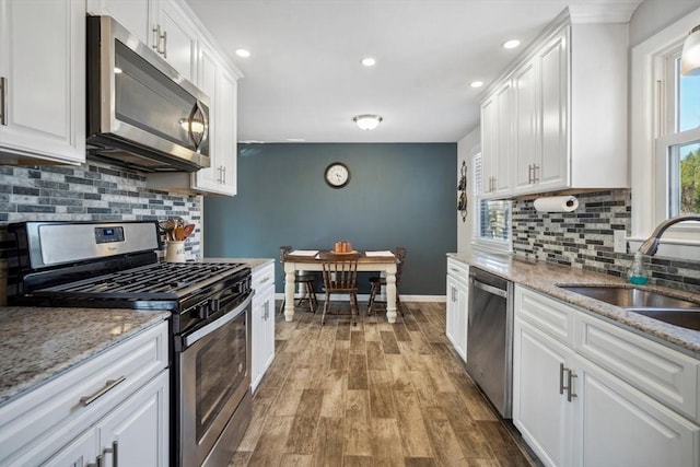 kitchen with a sink, wood finished floors, baseboards, white cabinets, and appliances with stainless steel finishes