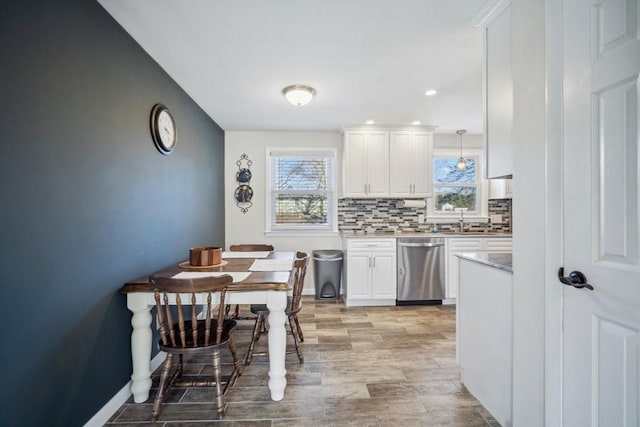 kitchen featuring stainless steel dishwasher, a sink, white cabinetry, and decorative backsplash