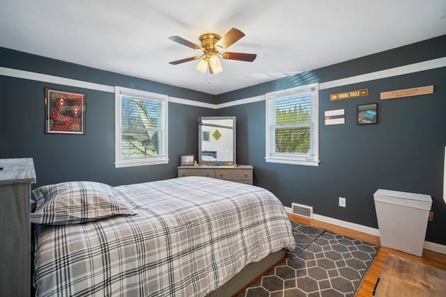 bedroom with a ceiling fan, visible vents, baseboards, and wood finished floors