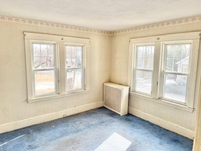 carpeted empty room featuring baseboards and radiator heating unit