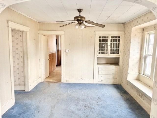 carpeted spare room featuring wallpapered walls, ceiling fan, and arched walkways