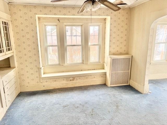 empty room featuring carpet floors, arched walkways, a ceiling fan, baseboards, and wallpapered walls