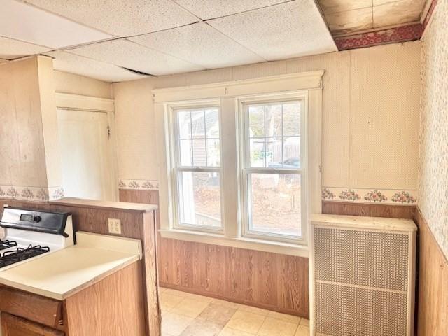 kitchen featuring range with gas stovetop, a paneled ceiling, light countertops, wood walls, and wallpapered walls