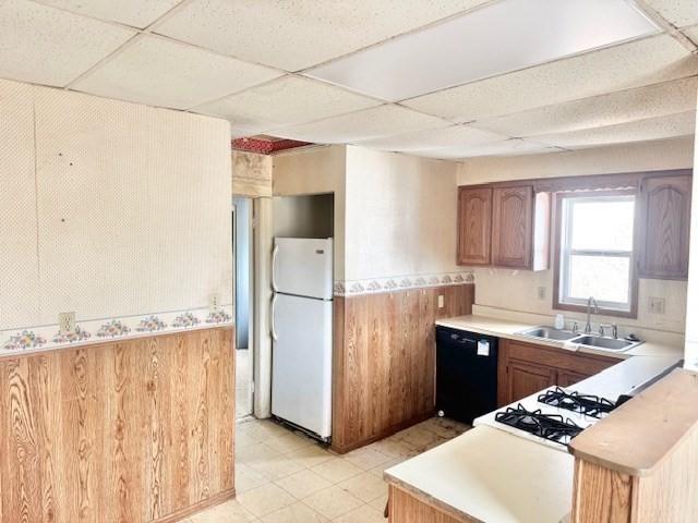 kitchen featuring black dishwasher, a paneled ceiling, a sink, and freestanding refrigerator