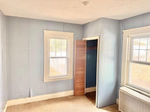 interior space with radiator, multiple windows, carpet floors, and a closet