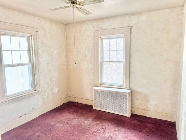 spare room featuring dark colored carpet, radiator heating unit, a ceiling fan, and baseboards