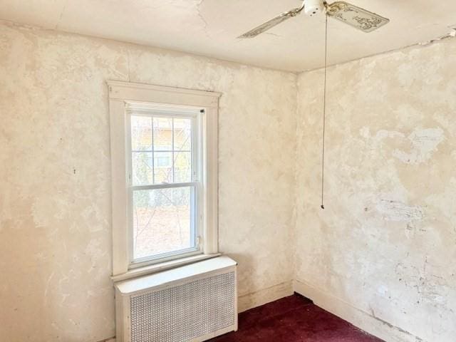 unfurnished room with radiator heating unit, a ceiling fan, and baseboards