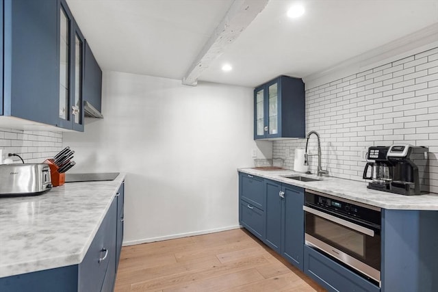 kitchen with tasteful backsplash, sink, oven, blue cabinetry, and light hardwood / wood-style flooring