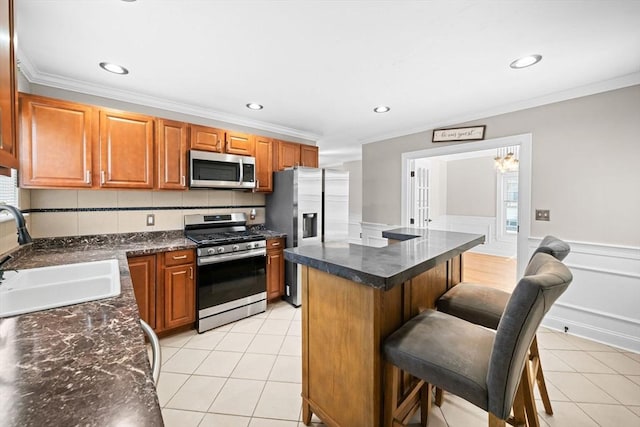 kitchen featuring light tile patterned flooring, wainscoting, stainless steel appliances, and a sink