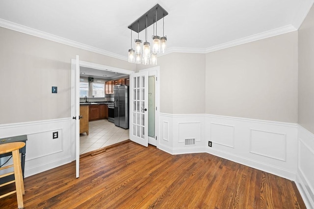 unfurnished dining area featuring french doors, visible vents, light wood-style flooring, and ornamental molding