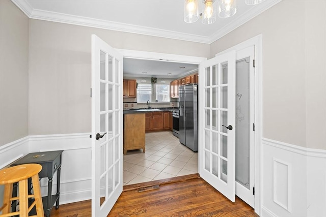 corridor featuring light wood-type flooring, a notable chandelier, ornamental molding, a sink, and french doors