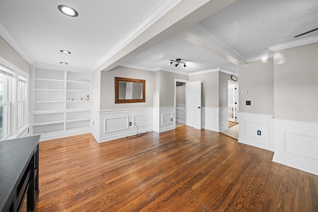 unfurnished living room featuring built in features, wainscoting, wood finished floors, and crown molding