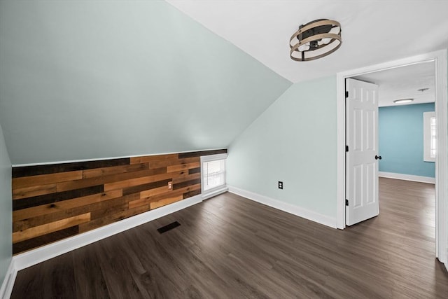 bonus room with visible vents, baseboards, dark wood-type flooring, and wood walls