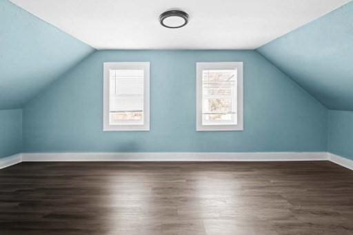 additional living space with baseboards, wood finished floors, and vaulted ceiling