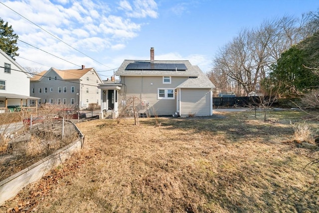 back of property with fence, solar panels, a vegetable garden, a yard, and a chimney