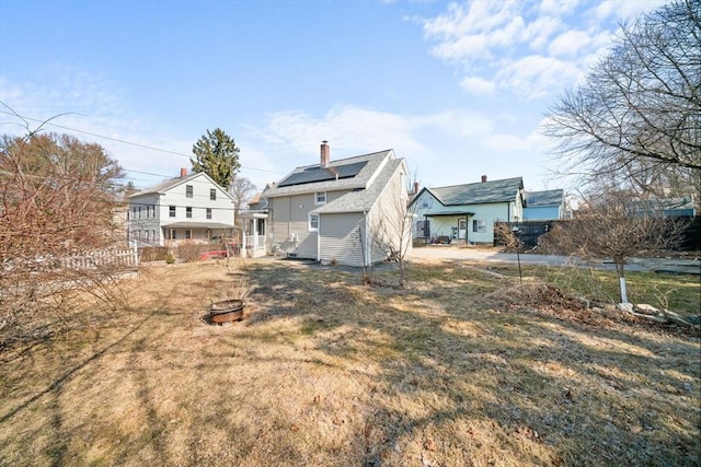 rear view of property with roof mounted solar panels, a chimney, and an outdoor fire pit