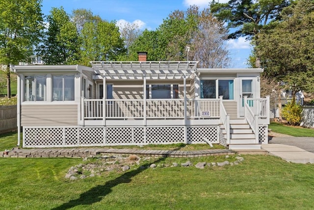 rear view of house featuring a pergola, a wooden deck, a chimney, a lawn, and a sunroom